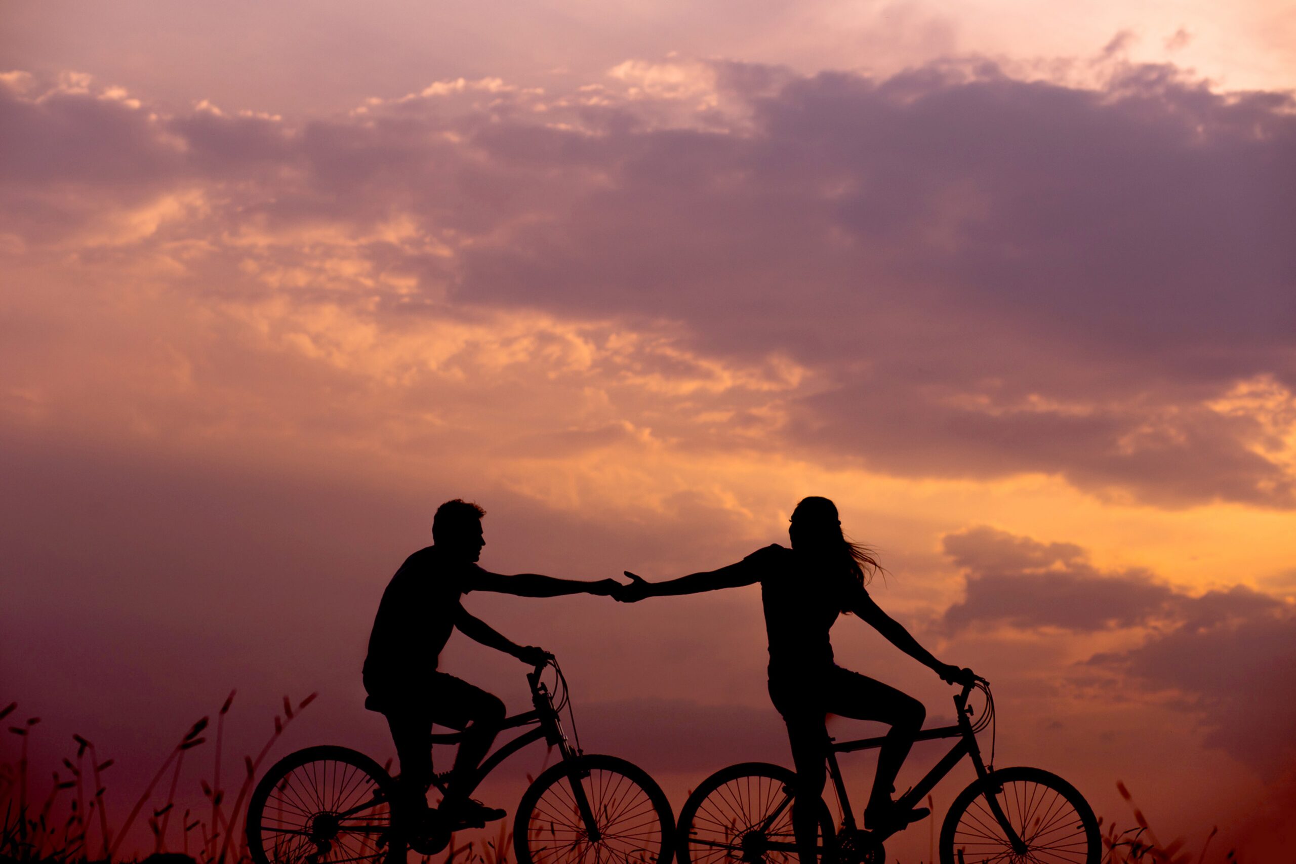 夕暮れの中自転車に乗って手をつなごうとする男女